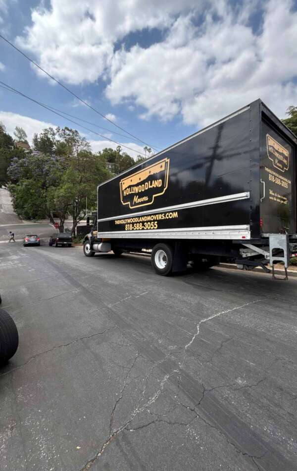 80254700307__E62768EB-1714-470E-982E-4C8EB03A7828 Hollywoodland Movers truck on a tree-lined street.